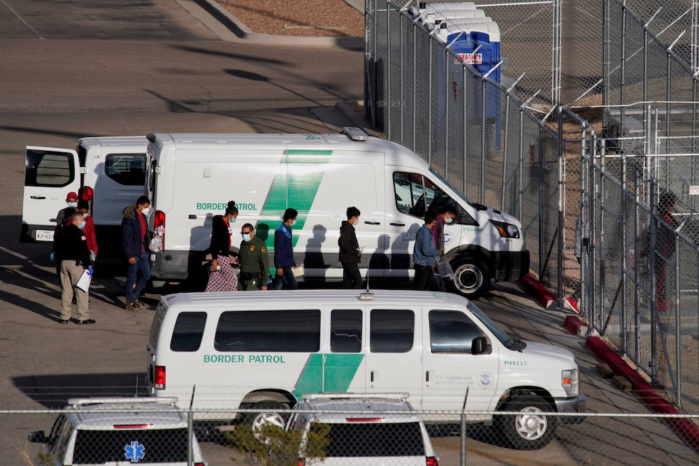 Vans from Border Patrol parked at a fence while people get out and walk