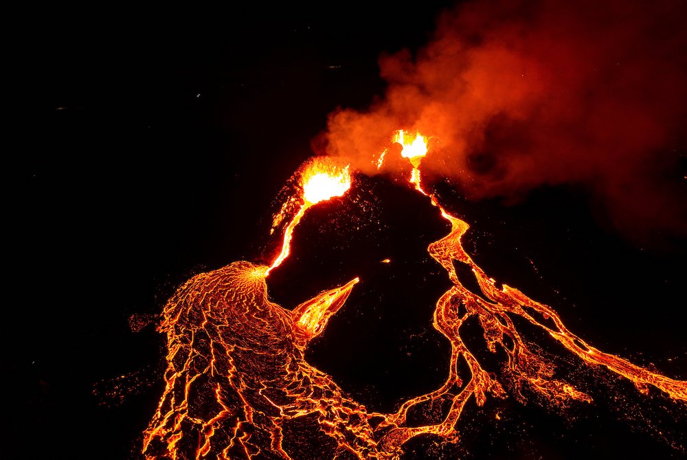 Orange lava flowing down dark volcano at night