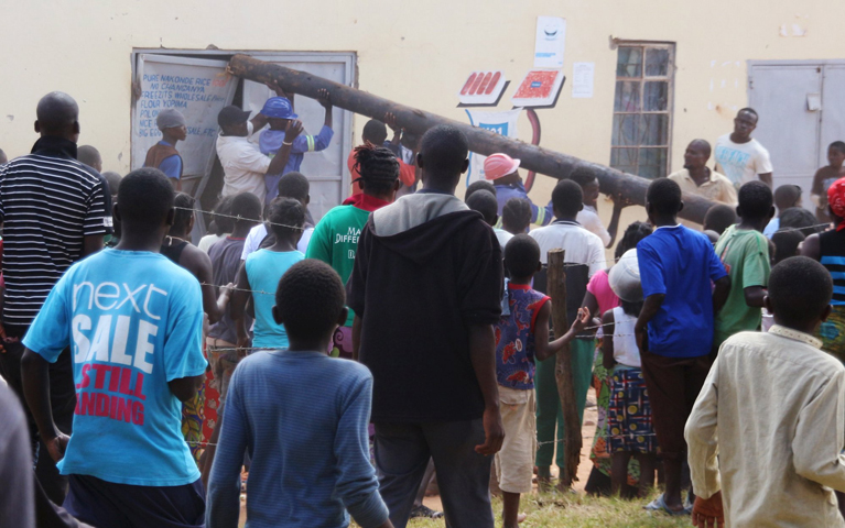 People use a pole to batter a shop doorway during clashes with police April 19 in Lusaka, Zambia. (CNS/Jean Mandela, Reuters)