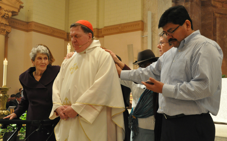 Deacon candidate Juan Carlos Ramirez, right, recites from a prayer card as he, Marie Tobin (Cardinal Joseph W. Tobin's mother), left, Domini Rouse and Benedictine Sister Jennifer Mechtild Horner lay their hands on Cardinal Tobin Dec. 3 in front of the altar at SS. Peter and Paul Cathedral in Indianapolis. Their prayers were part a prayer and blessing of the cardinal at a farewell Mass for him. (CNS photo/Natalie Hoefer, The Criterion)