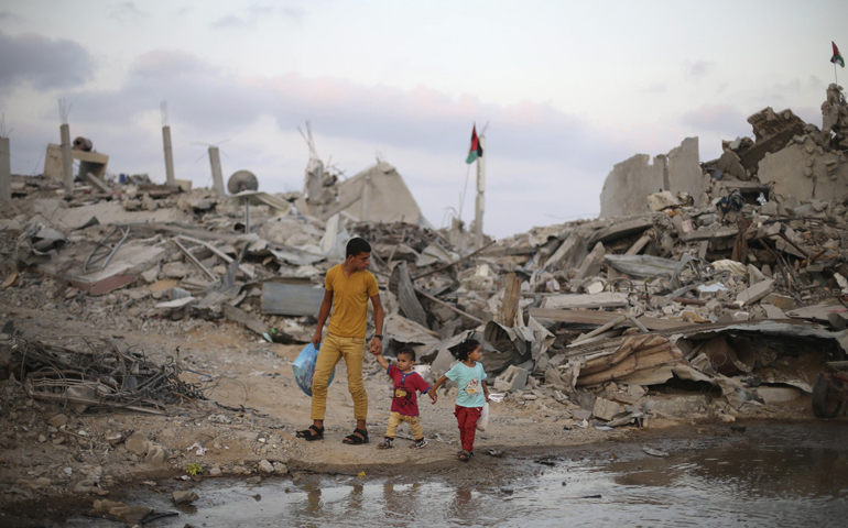 On Monday, the fifth day of cease-fire in Gaza, Palestinians in Gaza walk next to the ruins of houses destroyed during the Israeli offensive. (CNS/Reuters/Ibraheem Abu Mustafa)