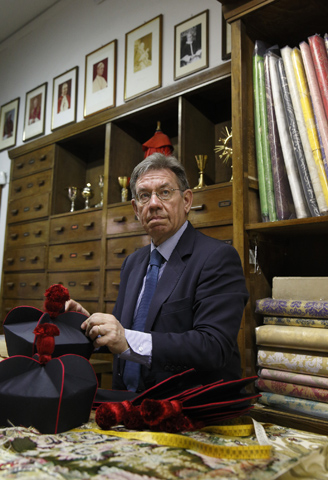 Photos of popes are displayed on the wall as an employee shows clerical wear to a customer at the Gammarelli clerical tailor shop in Rome in March 2013. (CNS/Paul Haring) 