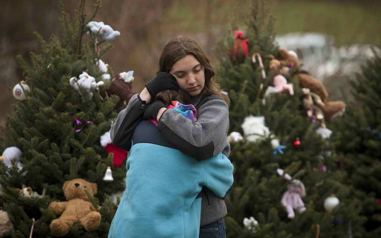 Two siblings hug in front of a row of Christmas trees lining the street near Sandy Hook Elementary School in Newtown, Conn., Dec. 16. Worshippers filled Sunday services to mourn the victims of a gunman's elementary school rampage that killed 20 children and six adults at the school Dec. 14. (CNS/Reuters)