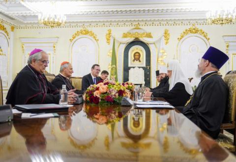 Dignitaries sit at table in gilded, rococo chamber. 