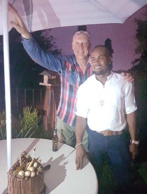 Two men posing together with a cake at a picnic table