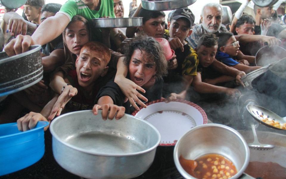 Children holding bowls and pots, their faces marred by deep anguish, clamor one over the other for the food.