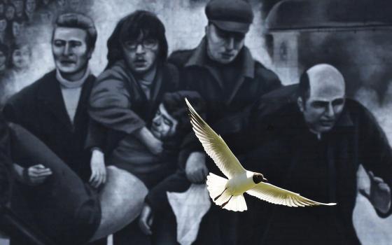 A seagull flies in front of a mural which shows a group of men, led by then-Fr. Edward Daly, right, carrying the body of shooting victim Jackie Duddy during 1972's Bloody Sunday in Derry, Northern Ireland. (CNS/Reuters/Cathal McNaughton)