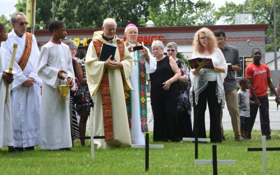 Fr. Victor Clore and members of Christ the King Parish in Detroit pause for a moment of silence July 22, 2017, in front of 44 crosses on the parish's front lawn, one for each of the lives lost in the city's violence of 1967. (CNS/The Michigan Catholic)