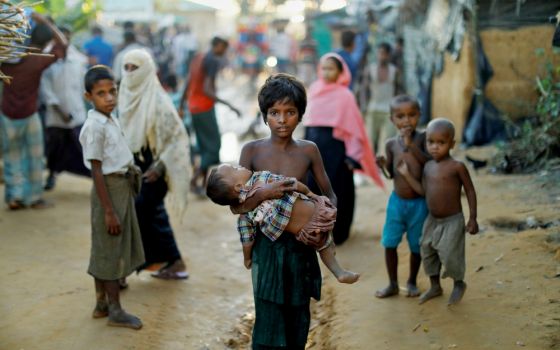 A young Rohingya refugee carries a child Oct. 10 while walking in a camp near Cox's Bazar, Bangladesh. (CNS/Reuters/Damir Sagolj)