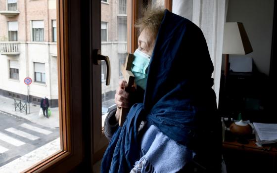 A woman wearing a protective face mask kisses a cross as she prays from the window of her home in Turin, Italy, March 25. (CNS/Reuters/Massimo Pinca)