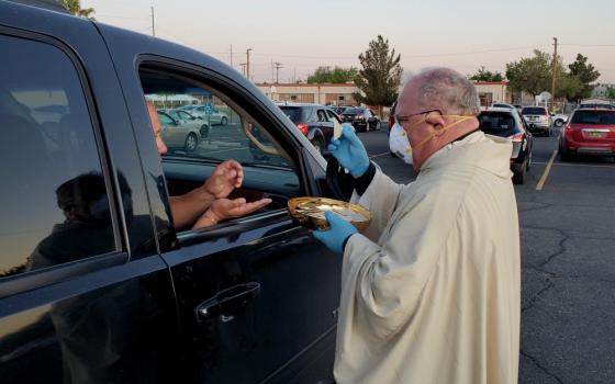 Bishop Peter Baldacchino wears a mask and gloves while giving Communion to a passenger of a vehicle during the Easter Vigil in the parking lot of the Cathedral of the Immaculate Heart of Mary in Las Cruces, New Mexico, April 11. (CNS)