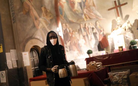 A volunteer carries coffee for people waiting for a free meal at the Church of Santa Anna in Barcelona, Spain, April 21, 2020, during the COVID-19 pandemic. (CNS/Reuters/Nacho Doce)