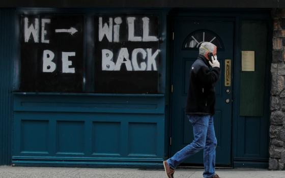 A man passes by a boarded-up restaurant in New York City April 29 with a sign suggesting it will reopen for business once it's safe in the coronavirus pandemic climate. (CNS/Reuters/Brendan McDermid)