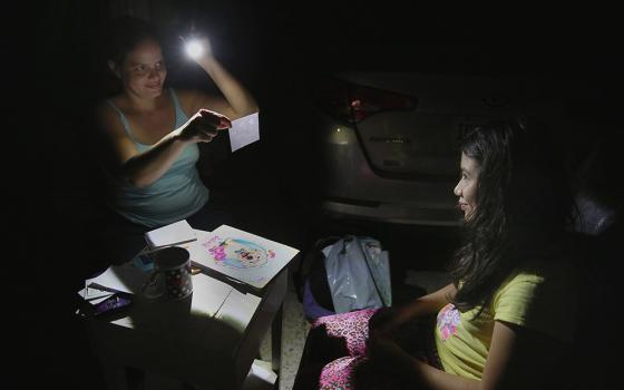 In this 2017 file photo, Margarita Rodriguez holds a flashlight as she quizzes her 11-year-old daughter Isel Martinez on homework outside their home in San Juan, Puerto Rico. (CNS/Bob Roller)