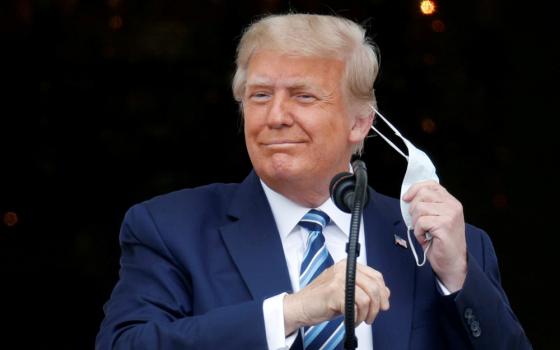 President Donald Trump takes off his face mask Oct. 10 as he comes out on a White House balcony in Washington to speak to supporters gathered for a rally on the South Lawn. (CNS/Reuters/Tom Brenner)