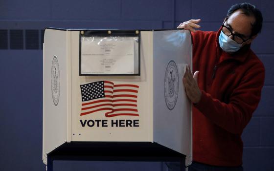 A man sanitizes a voting booth to fight the spread of the coronavirus disease at a polling station Oct. 25 on Staten Island, New York. (CNS/Reuters/Andrew Kelly)