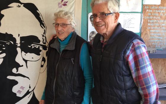 Mercy Sister Betty Campbell and Carmelite Fr. Peter Hinde pose next to an illustration of St. Oscar Romero in a 2019 photo in Ciudad Juarez, Mexico. Hinde died from complications due to COVID-19 Nov. 19, at the age of 97. (CNS/Julie Bourbon, courtesy of t