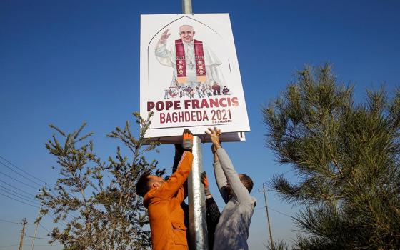 Volunteers secure a placard on a pole along a street in Qaraqosh, Iraq, Feb. 22. The placard shows the official logo, designed by Ragheed Nenwaya, for Pope Francis' planned March 7 visit to Qaraqosh, also known by its Aramaic name of Baghdeda.