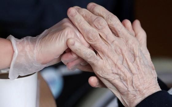 An employee holds the hand of a person at an elderly residence in Brussels April 14, 2020, during the COVID-19 pandemic. (CNS/Reuters/Yves Herman)