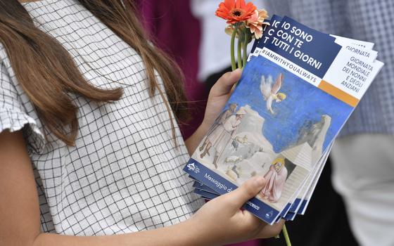 A young woman holds flowers and copies of Pope Francis' message for the first World Day for Grandparents and the Elderly. At the end of a Mass July 25 in St. Peter's Basilica at the Vatican, young people handed out flowers and copies of the message.