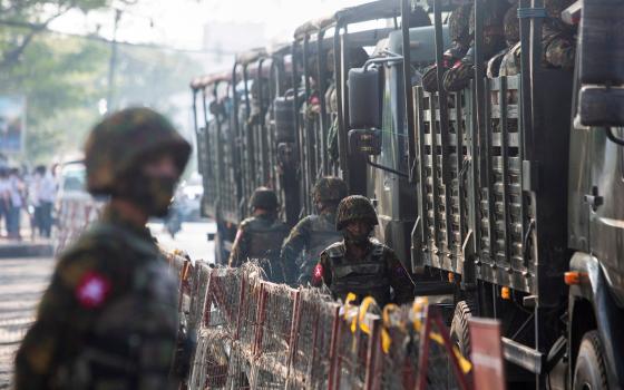 Soldiers stand next to military vehicles as people gather to protest the military coup in Yangon, Myanmar, Feb. 15, 2021. (CNS photo/Reuters)