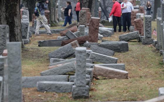 People walk in a cemetery full of toppled headstones