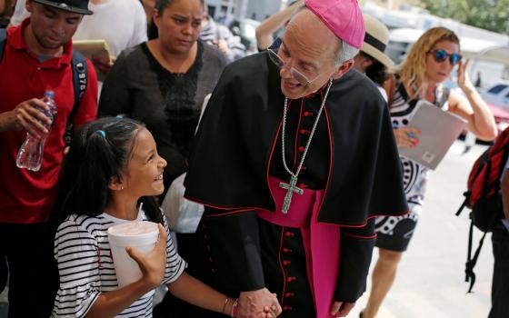 Bishop Mark J. Seitz of El Paso, Texas, shares a smile with a Honduran girl named Cesia as he walks and prays with a group of migrants at the Lerdo International Bridge in El Paso June 27, 2019. (CNS photo/Jose Luis Gonzalez, Reuters)