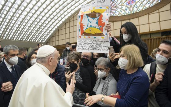 Pope Francis greets people near a banner in Italian calling for the pope's intervention with Russia, Ukraine and NATO, during his general audience in the Paul VI hall at the Vatican Jan. 19, 2022. (CNS photo/Vatican Media)