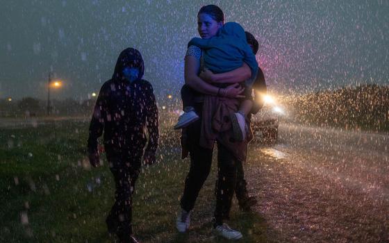 A mother from Central America and her three children are followed by a Texas Highway Patrol officer in La Joya, Texas, May 19, 2021, as they look for cover during a heavy rainfall after crossing the Rio Grande into the United States from Mexico. (CNS)