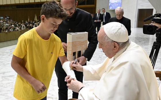 Pope Francis autographs the cast of a boy during his general audience in the Paul VI hall at the Vatican Aug. 31, 2022. 