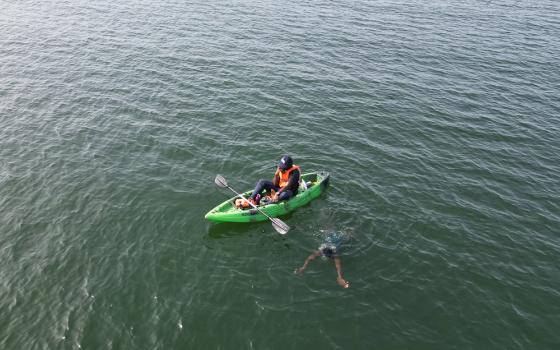 A member of the Agbetsi Living Water Swim expedition crew radios other crew members with a status update while paddling alongside Yvette Tetteh as she swims in the Volta River in Ghana. (Courtesy of the Or Foundation)