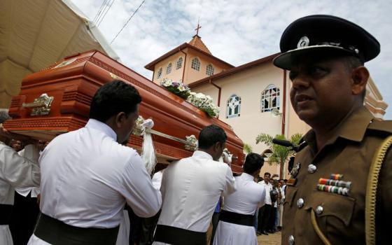 Member of military stands as pallbearers wearing white carry coffin.