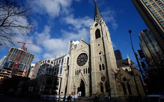 A Cathedral and its spire stretches into the sky with other high rises surrounding it