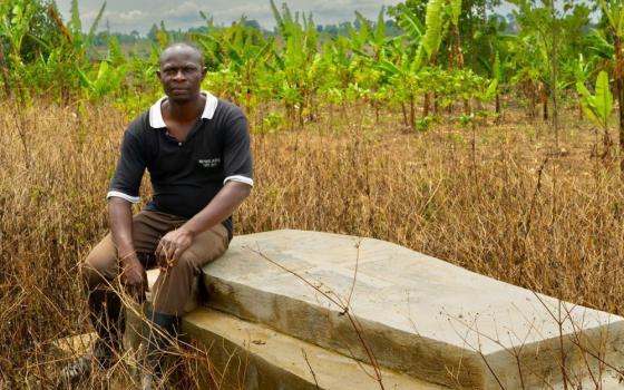 Man sits on a grave that is covered with a cement or stone box.