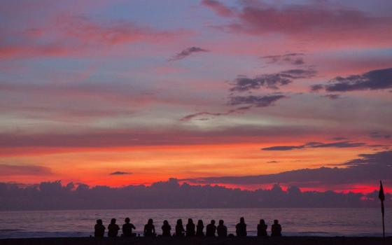 Silhouette of people in front of a lake and mountains at sunset. (Photo by Cristina Cerda/Unsplash/Creative Commons)