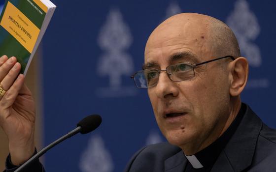 Cardinal Víctor Manuel Fernández, prefect of the Dicastery for the Doctrine of the Faith, holds up a copy of the dicastery's declaration, Dignitas Infinita ("Infinite Dignity") on human dignity during a news conference April 8 at the Vatican press office. (CNS/Pablo Esparza)