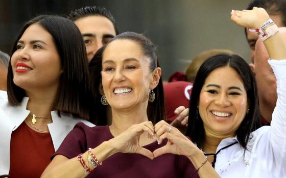 Scheinbaum smiles and makes a heart shape with her hands. 