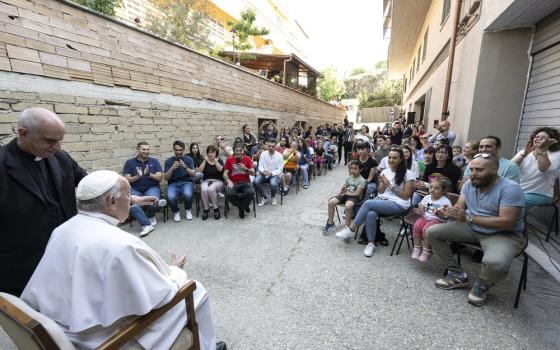 Pope Francis, seated, pictured from behind facing apartment residents in brick courtyard