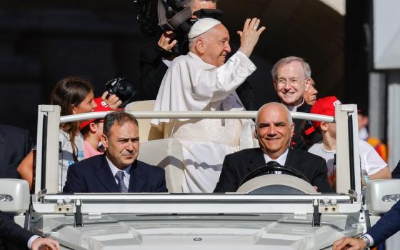 Pope Francis, standing in popemobile and framed by driver and attendants, waves to crowds