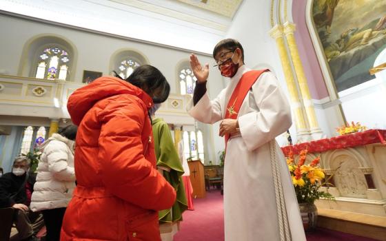 Deacon, vested, makes sign of cross over woman with head bowed.