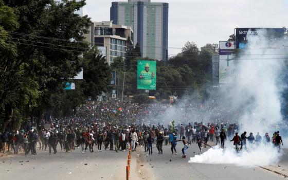 Enormous assembly marches through wide boulevard as smoke rises from street.