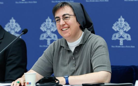 Sister Smerilli smiles as she sits and listens at panel desk. 