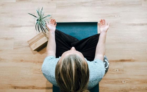 woman sits on cushion, with hands pointing upward