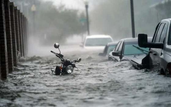 Flood waters rush through nearly submerged vehicles in street