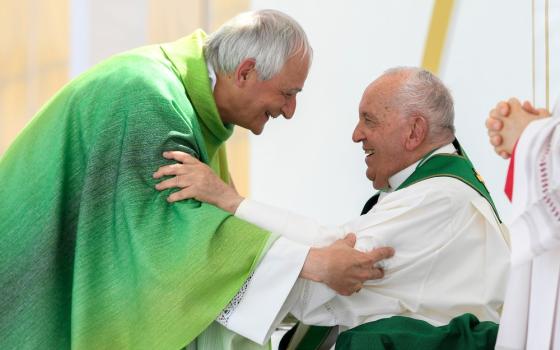 Zuppi, vested, bends to Francis, seated, as the embrace each other.