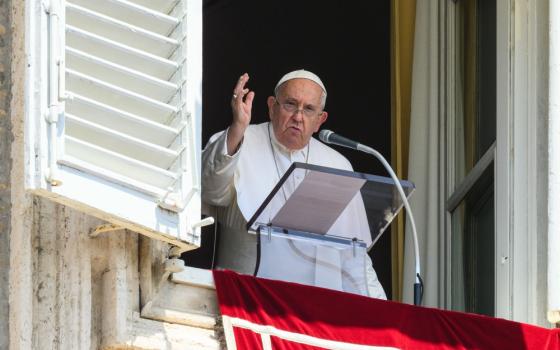 Pope Francis raises hand in blessing, standing at a lectern on the balcony in St. Peter's Square. 