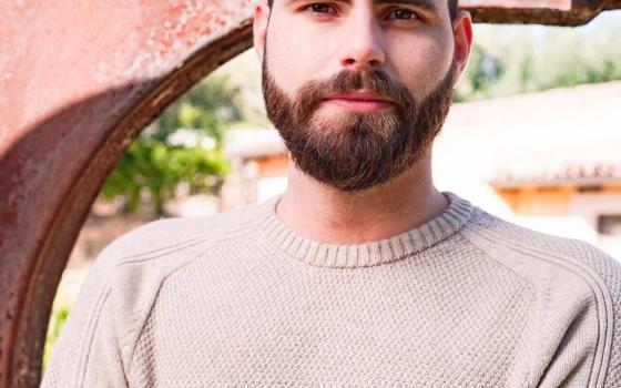 Outdoor, natural-lit headshot of Messina, arms folded, looking at camera. 