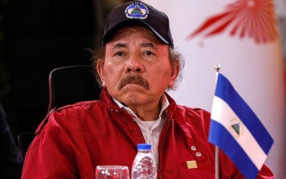 Ortega, seated, wears windbreaker and ball cap. 