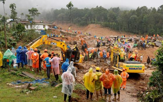 Group of people wearing rain ponchos stand around search site along with earth movers. 