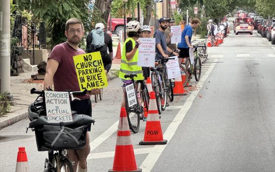 People with bikes and protest signs stand in a lane demarcated by traffic cones. 